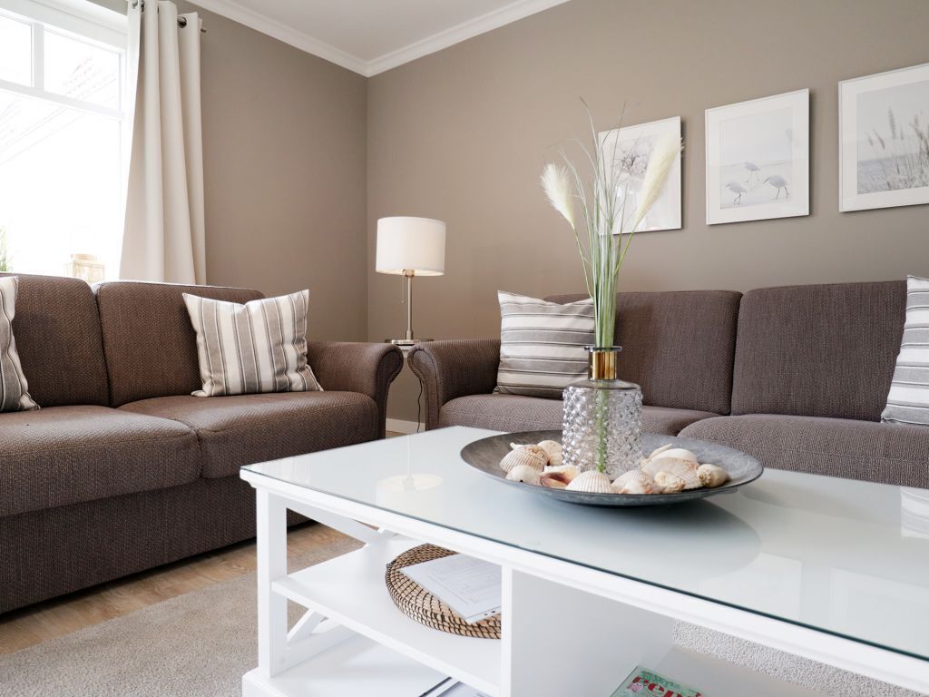 A living room with a glass coffee table, two brown sofas, a lamp, and framed artwork on the wall.