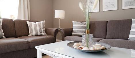 A living room with a glass coffee table, two brown sofas, a lamp, and framed artwork on the wall.