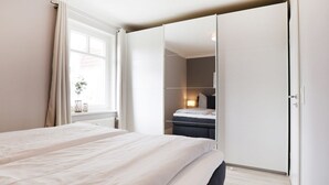 Ett modernt sovrum med en stor säng, en garderob och ett fönster med gardiner.