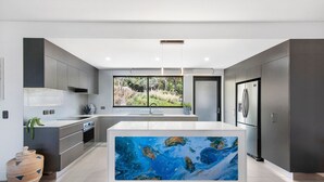 A modern kitchen with a large island, stainless steel appliances, and a view of greenery outside. - Valle Vista Luxury Apartments (Redlynch)