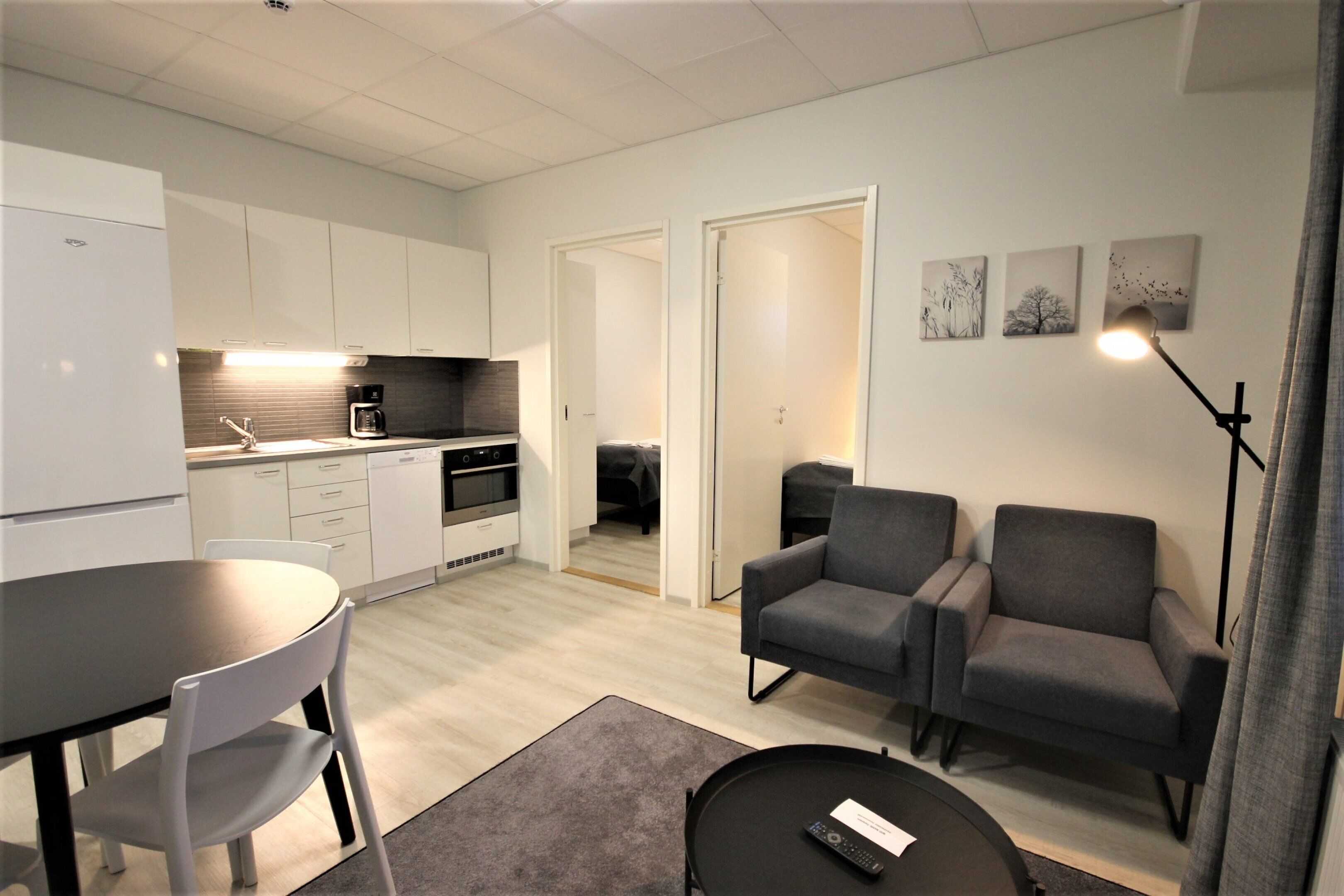 A modern kitchen with white cabinets, a dining table with chairs, a sofa, and a remote control on a coffee table.