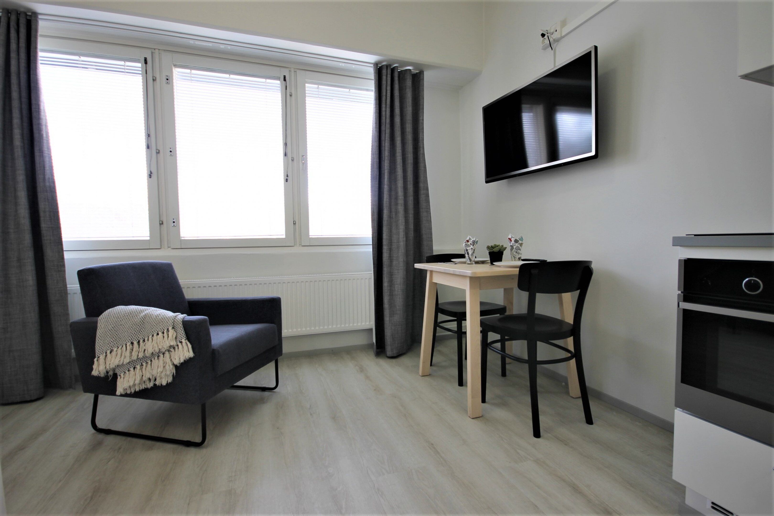 A modern room with a sofa, a small table, two chairs, a TV, and a built-in oven.