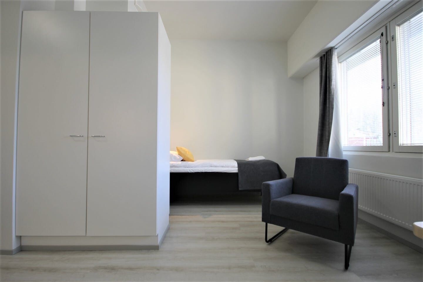 A bedroom with a bed, a wardrobe, a chair, and a window with blinds.