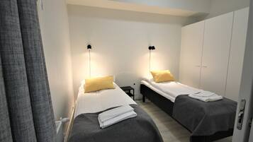 Een hotelkamer met twee eenpersoonsbedden, elk met een kussen en dekbed. Tussen de bedden staat een klein tafeltje, en er is een kledingkast op de achtergrond te zien.