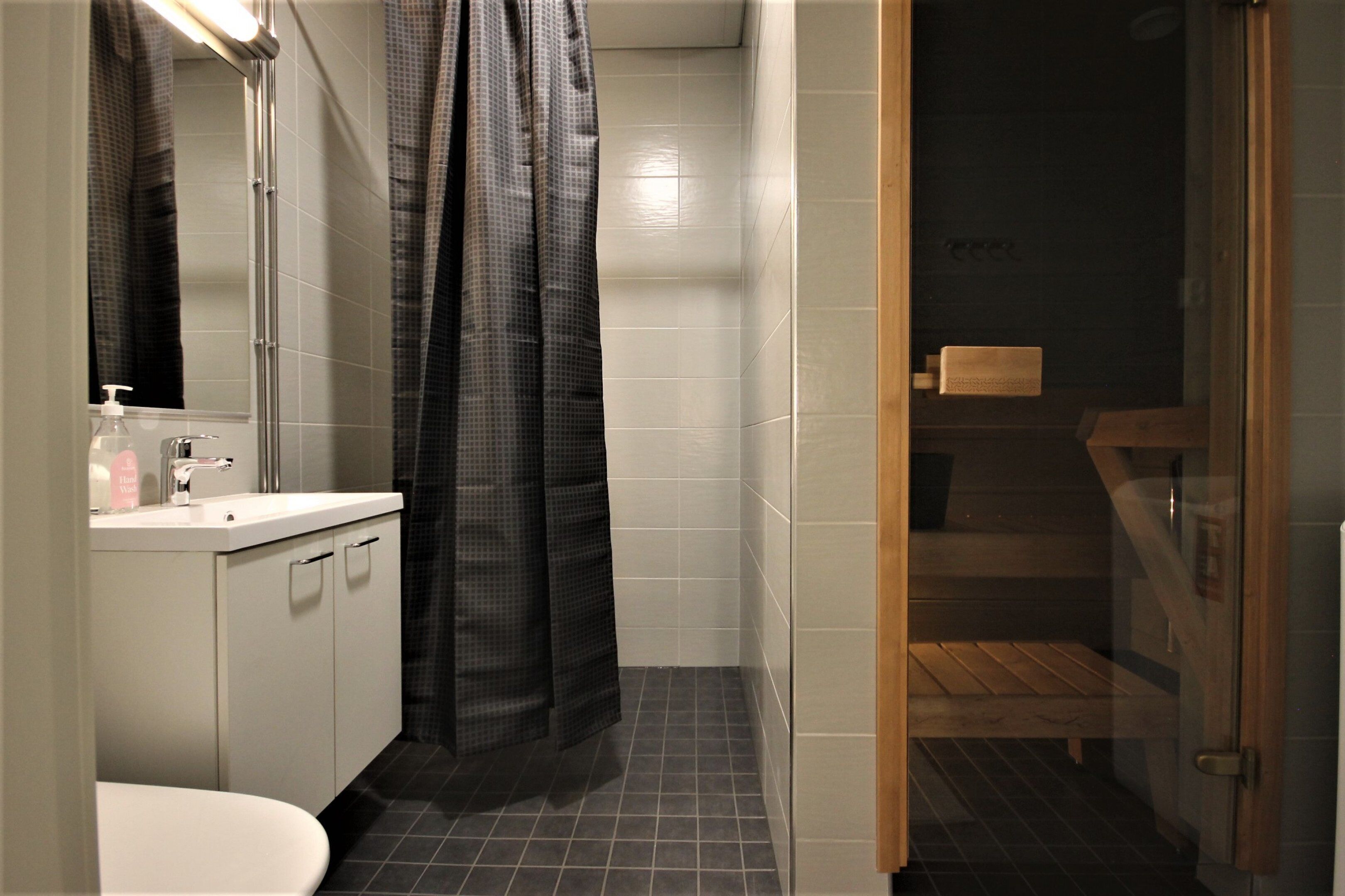 A bathroom with a white sink, a mirror, a shower curtain, and a wooden bench.