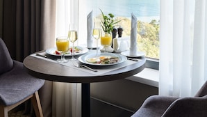 A dining area with a table set for two, a view of the sea, and a window with curtains. - Premier Hotel Odesa (Odesa)