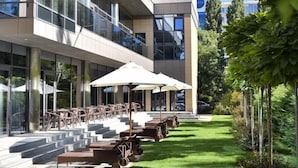 A modern building with a glass facade, outdoor seating area with umbrellas, and a well-maintained lawn. - Premier Hotel Odesa (Odesa)