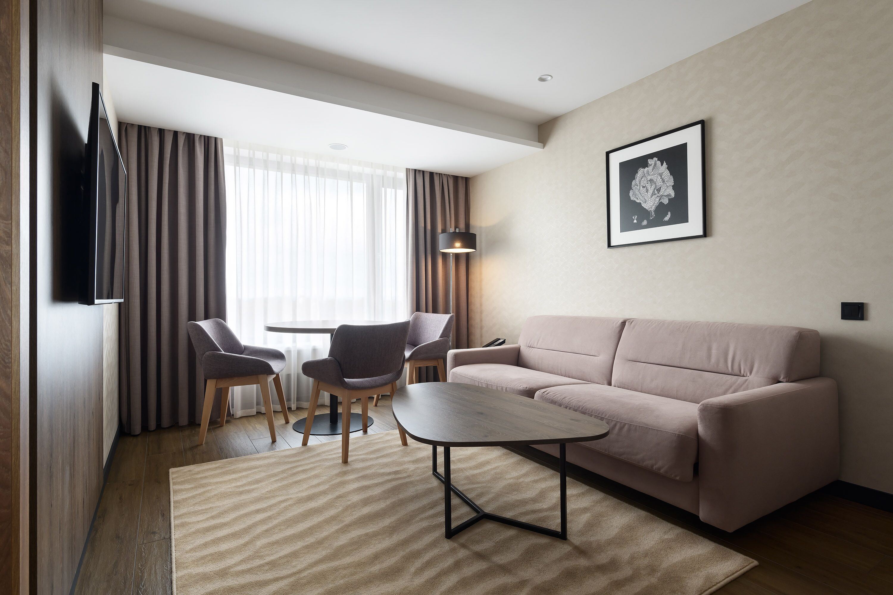 A modern hotel room with a sofa, a small table, two chairs, a TV, and a framed picture on the wall.