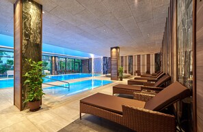Een moderne binnenzwembadruimte met loungebedden en een groot waterkunstwerk.