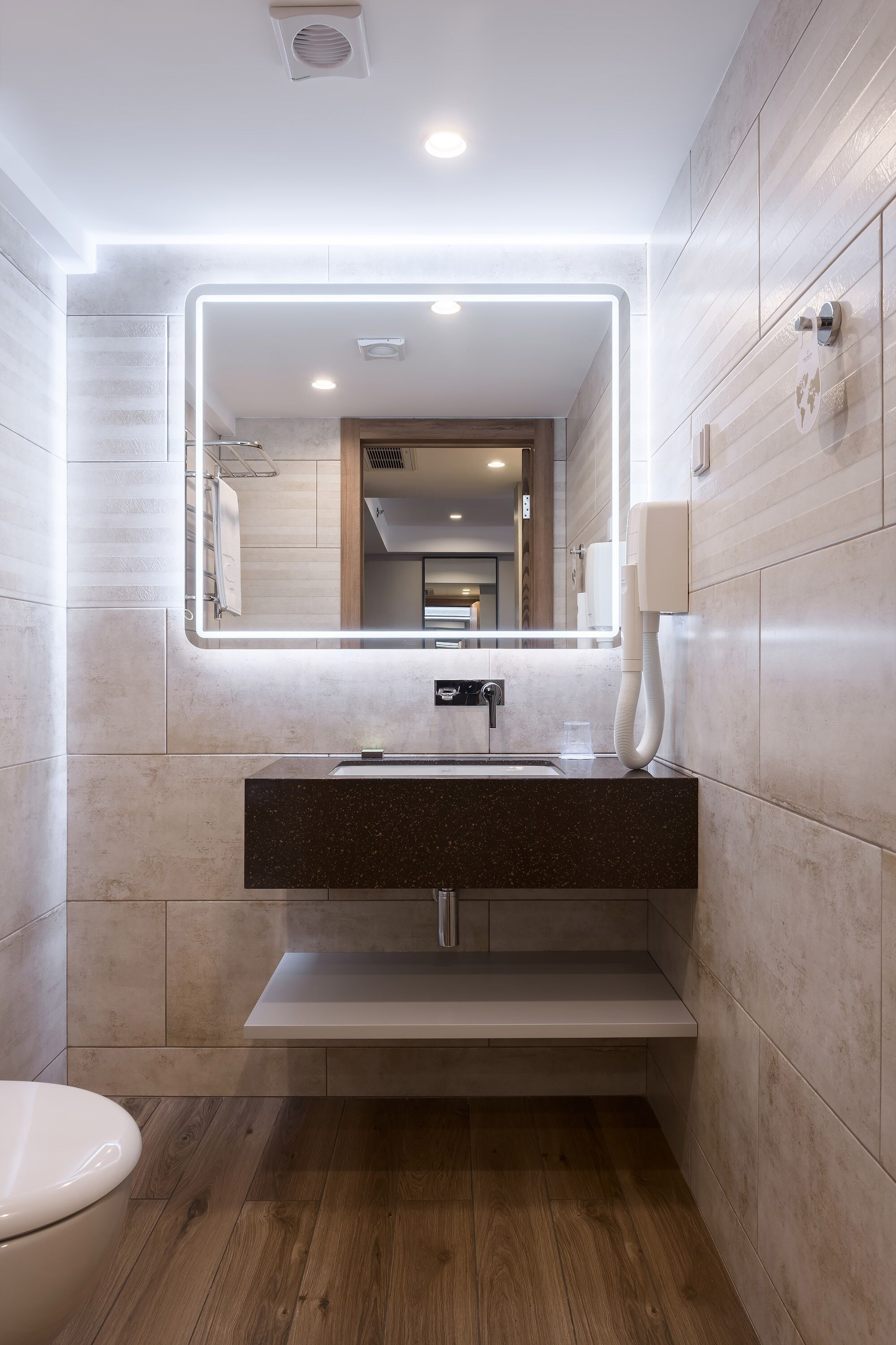 A modern bathroom with a large mirror, a sink, and a toilet.