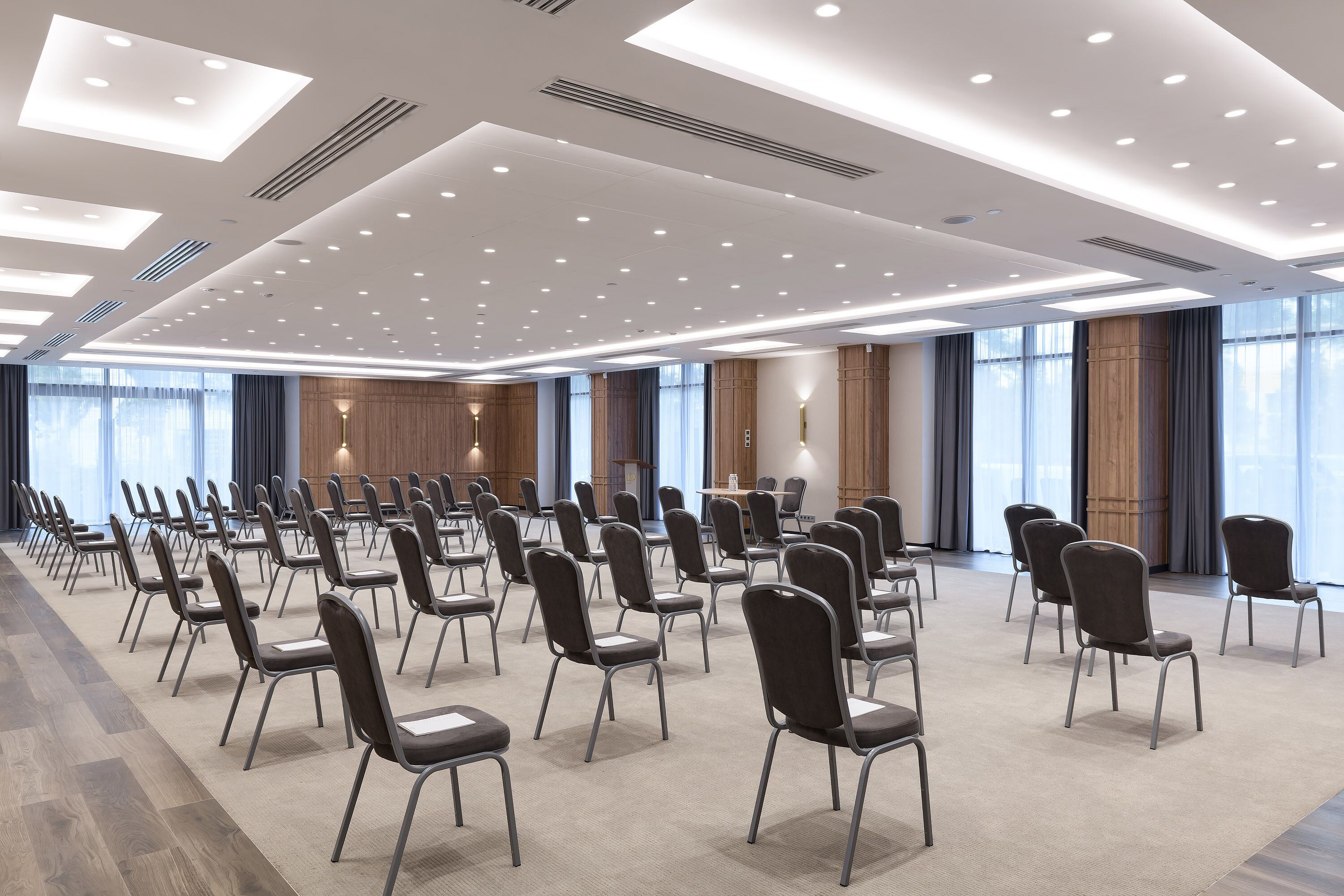 Un salón de conferencias con filas de sillas, una mesa grande y ventanas amplias.