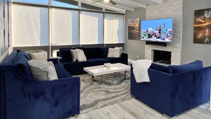 Ein modernes Wohnzimmer mit einer blauen Sofagarnitur, einem weißen Couchtisch und einem flachbildfernseher an der Wand.
