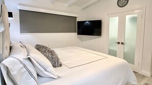 Ein Schlafzimmer mit einem Bett, einem Deckenventilator, einem an der Wand befestigten Fernseher und einer Tür mit satinierten Glasscheiben.