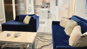 Ein modernes Wohnzimmer mit zwei blauen Sofas, einem Couchtisch und einer Küche im Hintergrund.