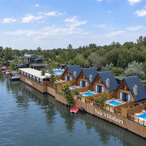 A waterfront property with wooden cabins, a pool, and a restaurant.