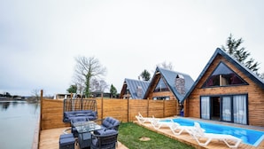 Una terraza de madera con mobiliario exterior, una piscina y vistas a un lago.