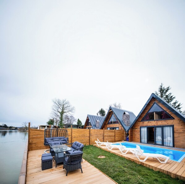 A wooden deck with outdoor furniture, a swimming pool, and a view of a lake.