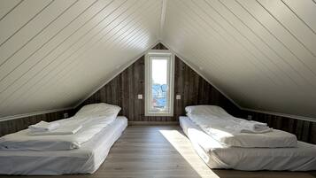 Habitación tipo dormitorio con dos camas individuales, suelo de madera y techo inclinado con tragaluz.