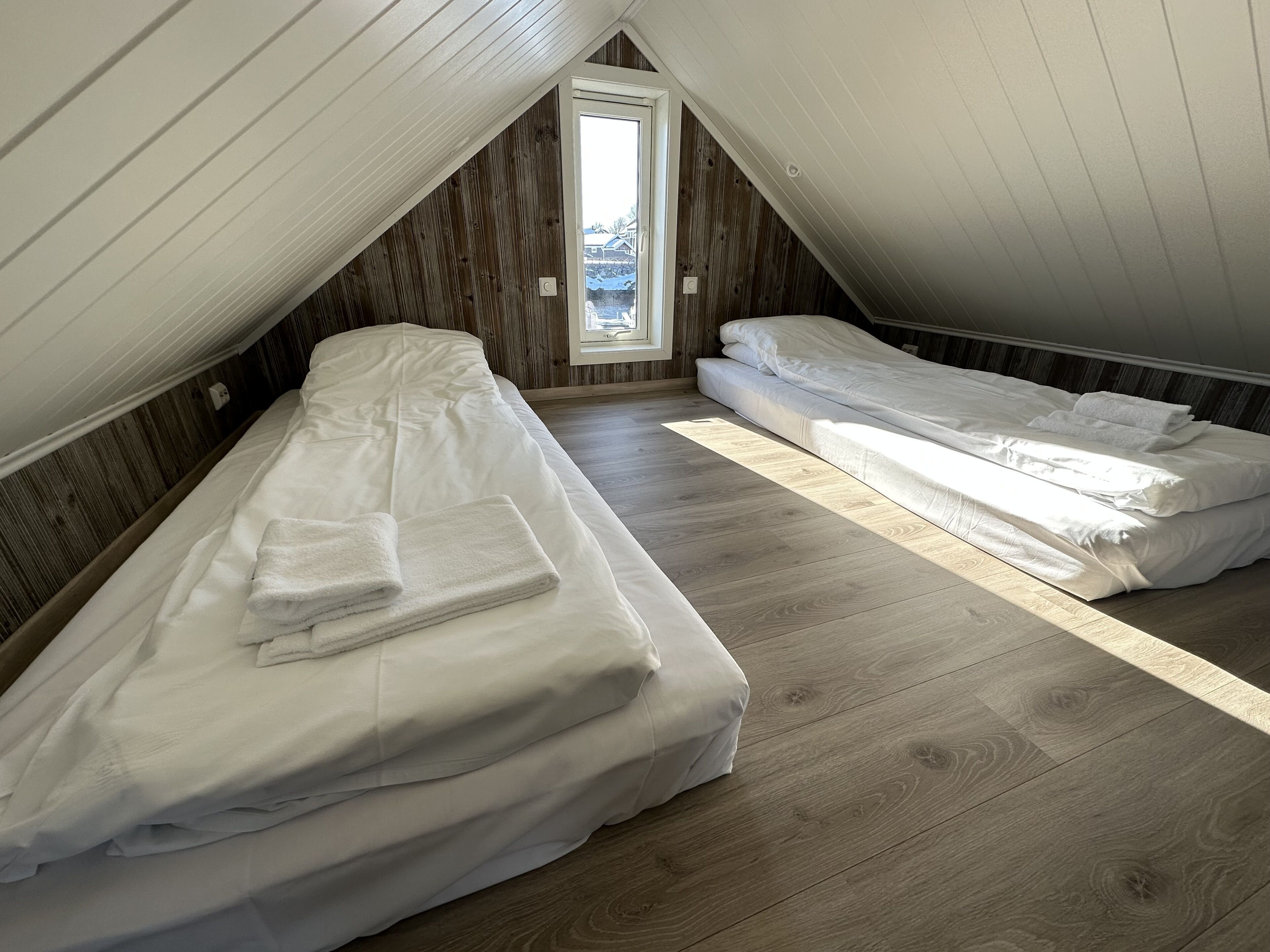 A small attic bedroom with two beds, wooden flooring, and a sloped ceiling.