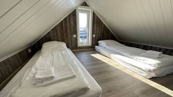 A small attic bedroom with two beds, wooden flooring, and a sloped ceiling.