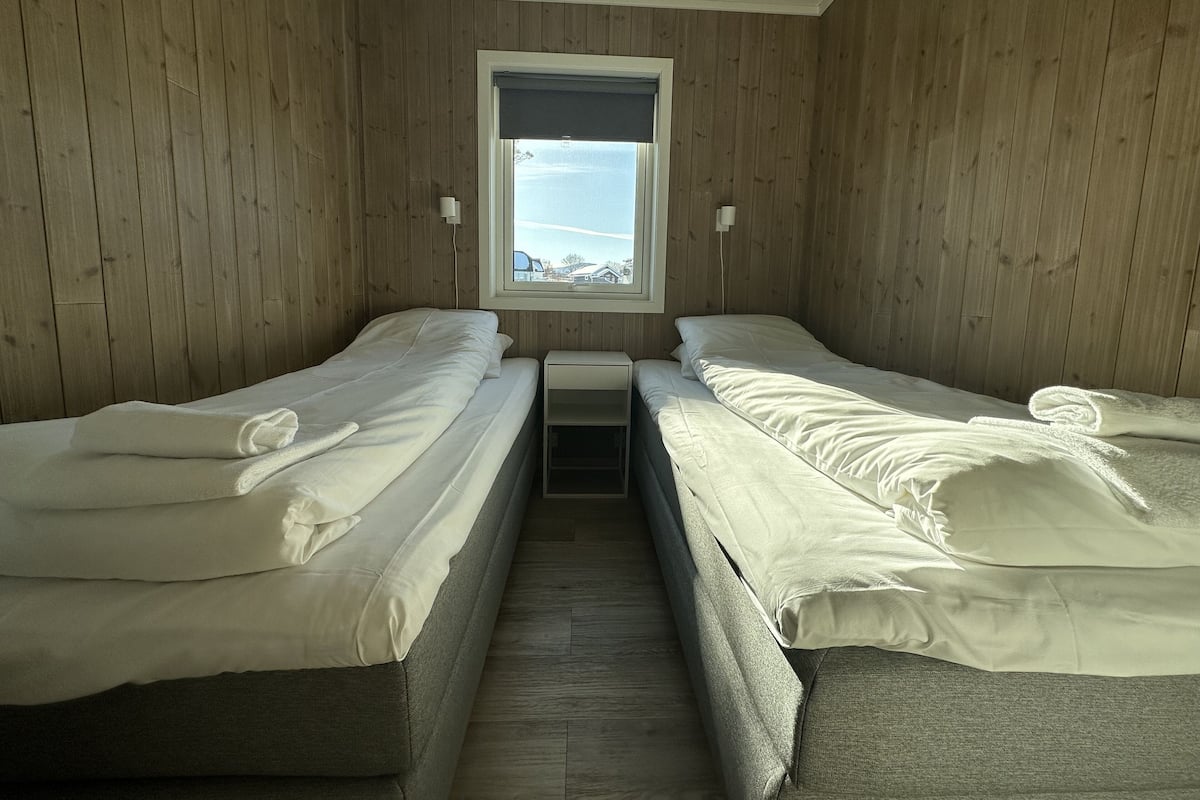 Quarto com duas camas de solteiro, uma janela pequena e paredes de madeira.