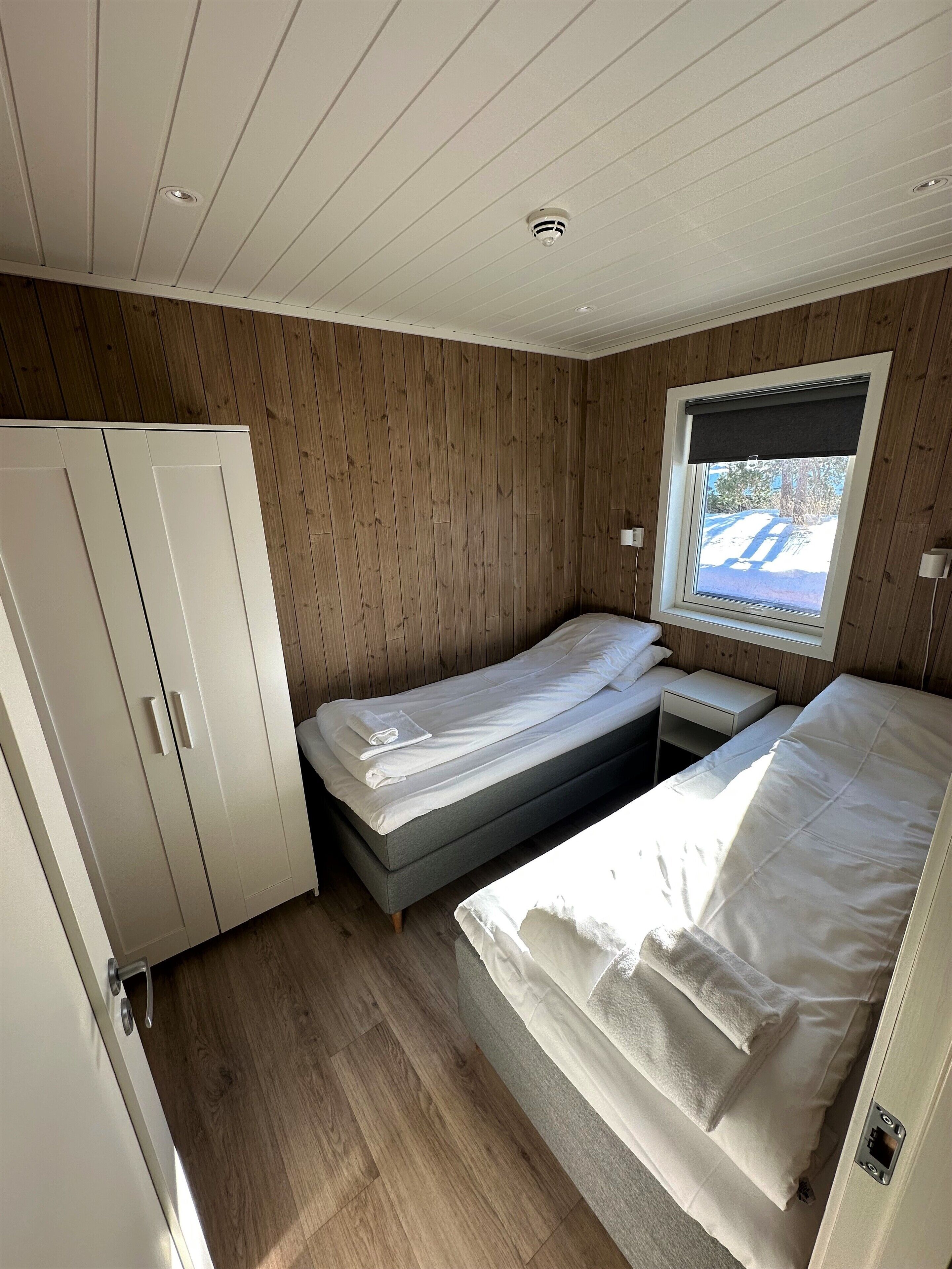 A bedroom with two beds, a wardrobe, a window with a view, and a ceiling light.