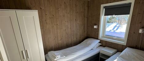 A bedroom with two beds, a wardrobe, a window with a view, and a ceiling light.