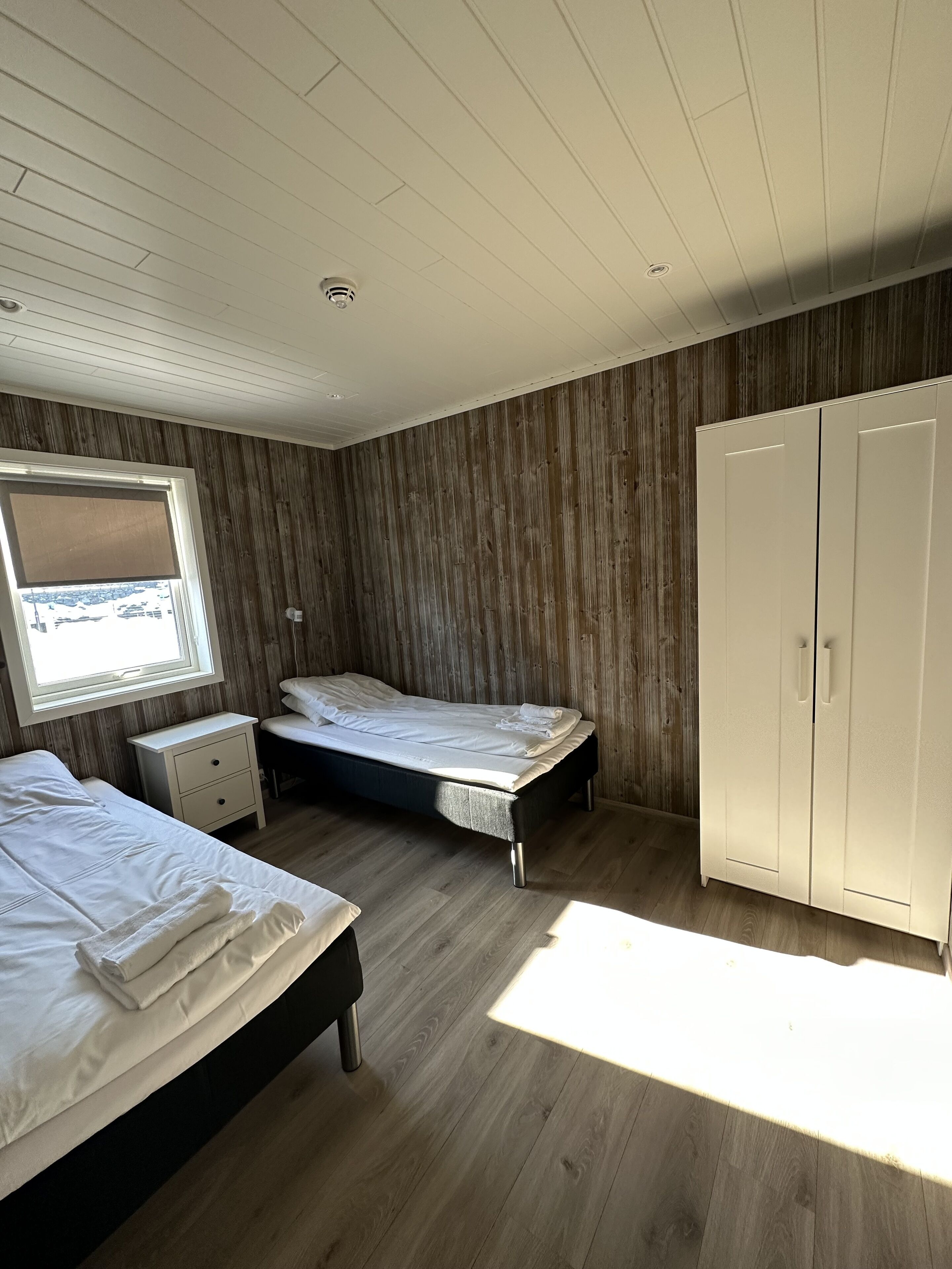 Makuuhuoneessa on kaksi sänkyä, vaatekaappi, ikkuna, jossa on sälekaihtimet, ja kattovalaisin.
