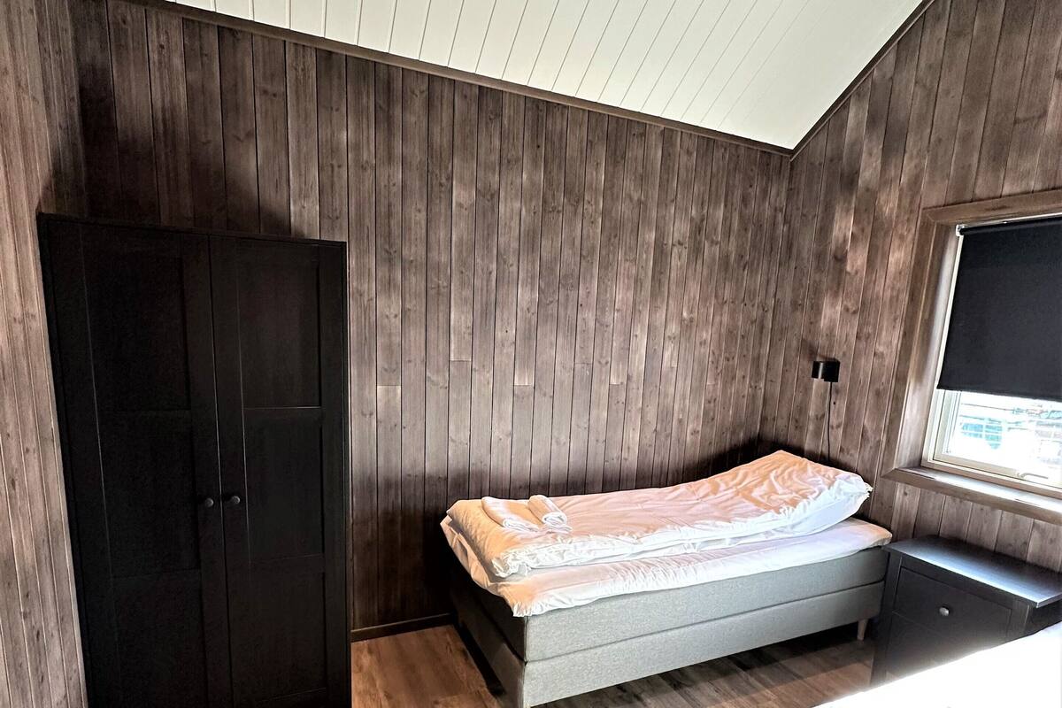 Quarto com teto inclinado, cama, guarda-roupa e janela.