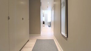 Un couloir doté d’un parquet en bois clair, d’un tapis gris et d’un grand miroir sur le mur de droite.