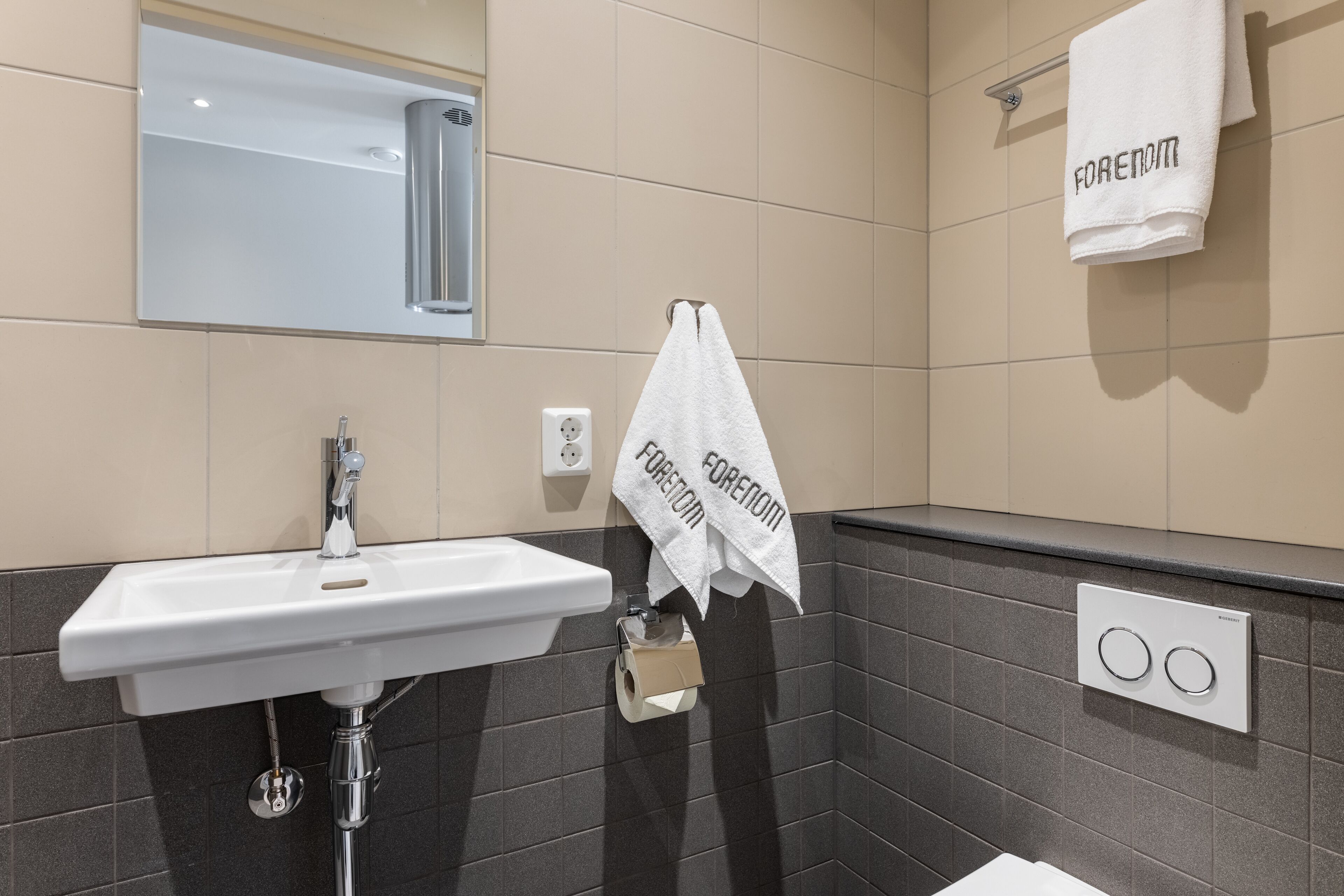Un baño moderno con un lavabo blanco, un espejo encima y dos toallas colgadas en un tendedero.