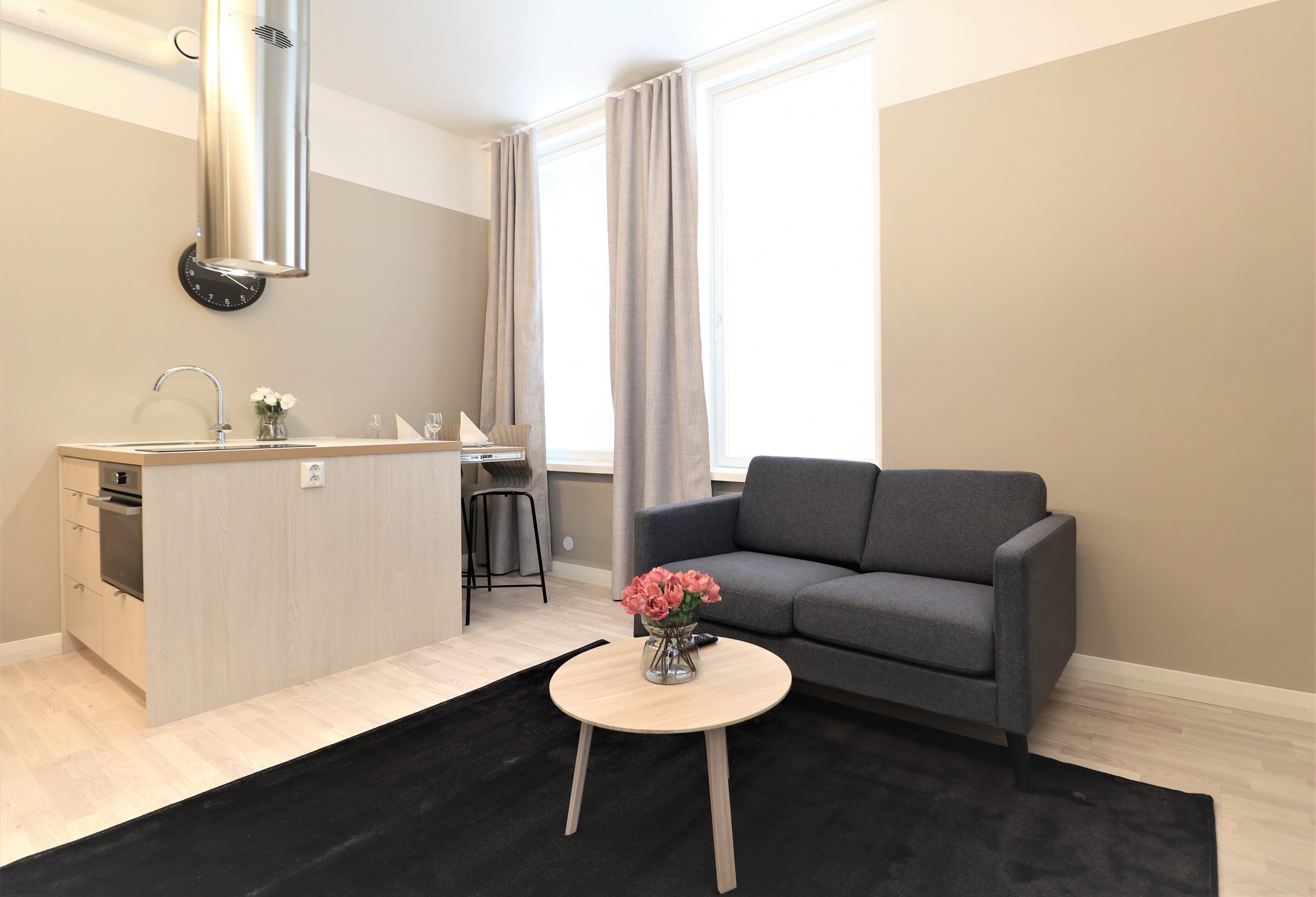 A modern kitchen with a built-in stove, a dining area with a grey sofa, and a small round table with a vase of flowers.