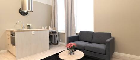 A modern kitchen with a built-in stove, a dining area with a grey sofa, and a small round table with a vase of flowers.