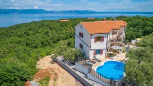 Ein zweistöckiges Haus mit Swimmingpool, umgeben von üppiger Vegetation und mit Blick auf ein großes Gewässer.
