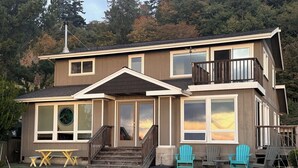 Une maison à deux étages dotée d’un balcon, de grandes fenêtres et d’une terrasse en bois.