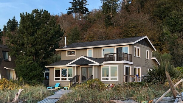 Une maison à deux étages dotée d’un balcon, de grandes fenêtres et d’une terrasse.