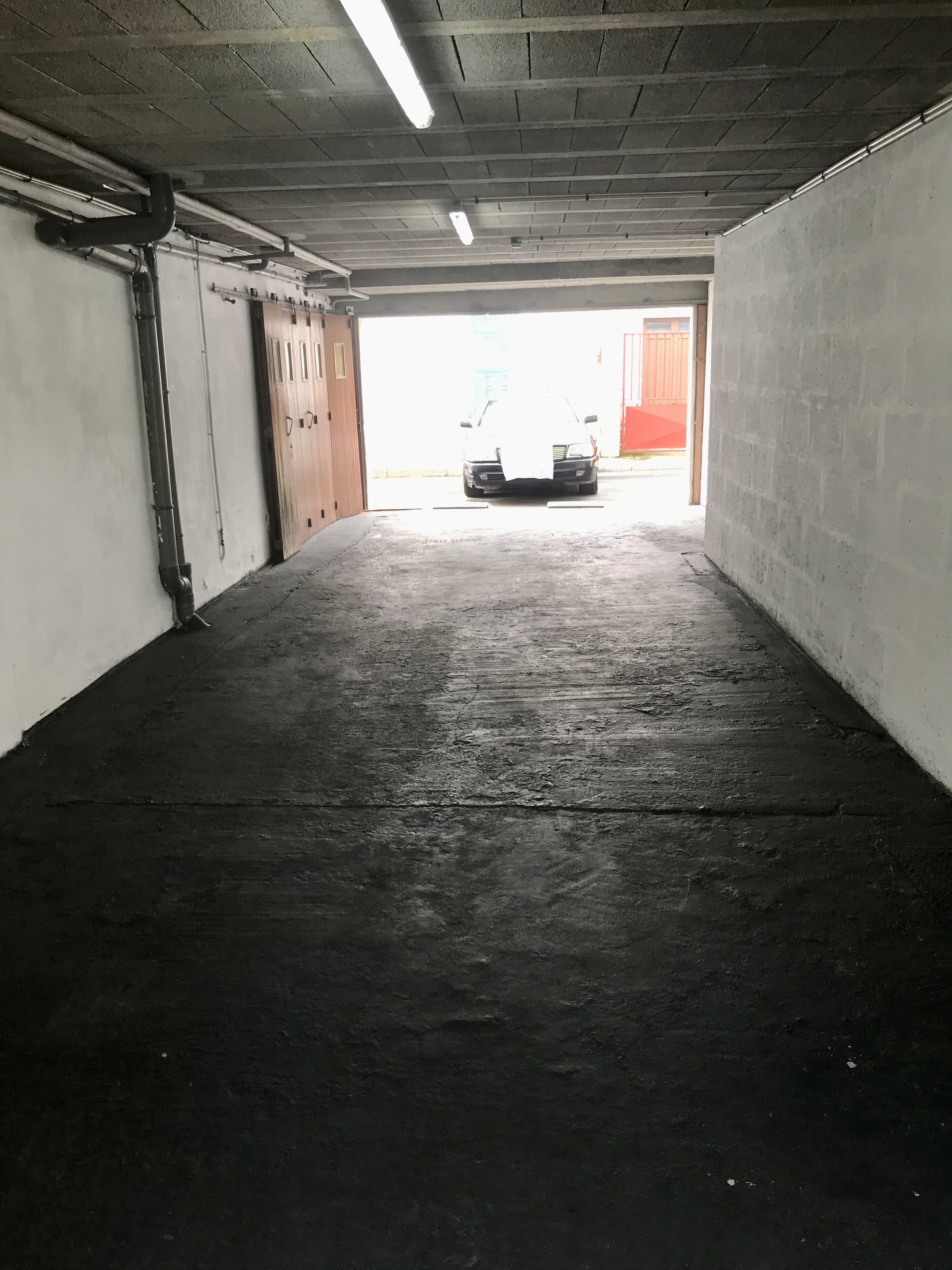 Autotalli, jossa on betonilattiat ja -seinät, loisteputkivalaistus ja yksi auto pysäköitynä sen päätyyn.