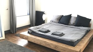 Quarto moderno com cama de plataforma de madeira, roupa de cama cinza e tapete cinza.