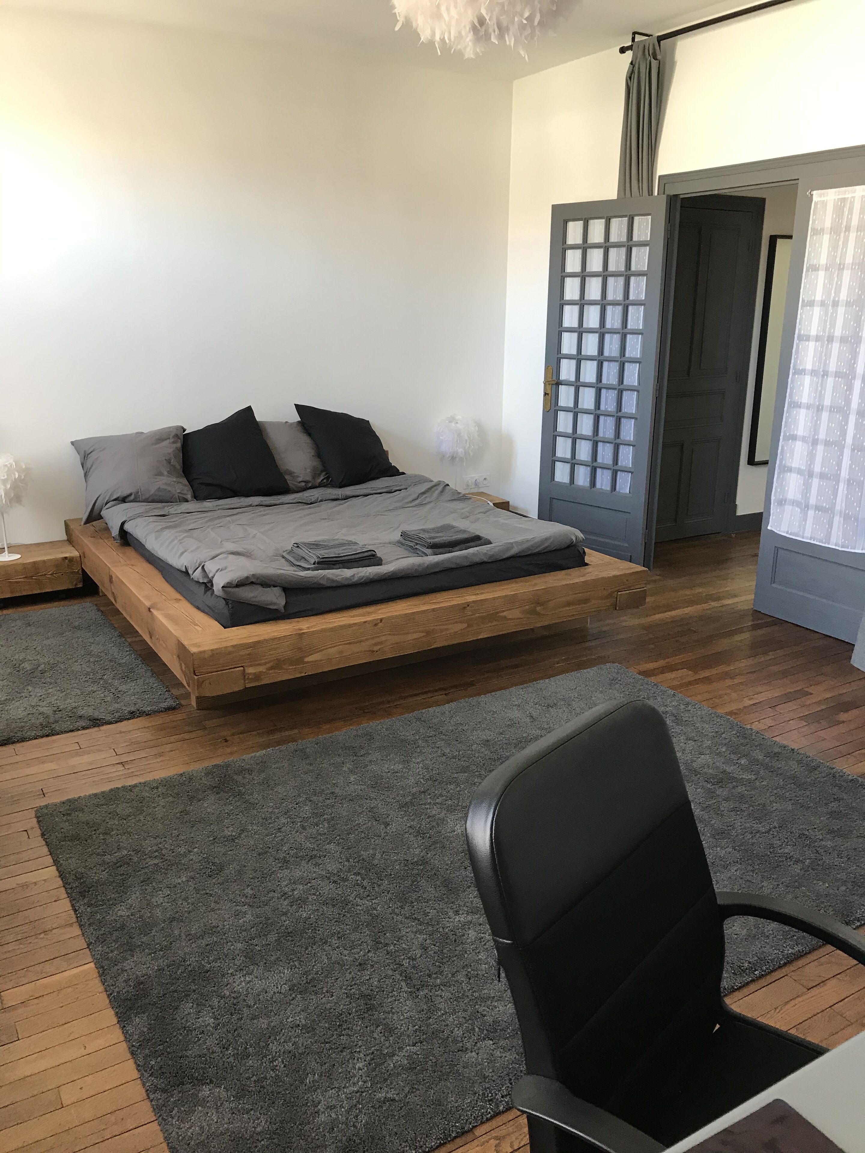 Ein modernes Schlafzimmer mit einem Holzbett, grauer Bettwäsche, einem schwarzen Stuhl und einem grauen Teppich.