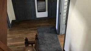 Uma escada de madeira com um patamar revestido de carpete, uma porta escura e uma pequena janela com vista para o exterior.