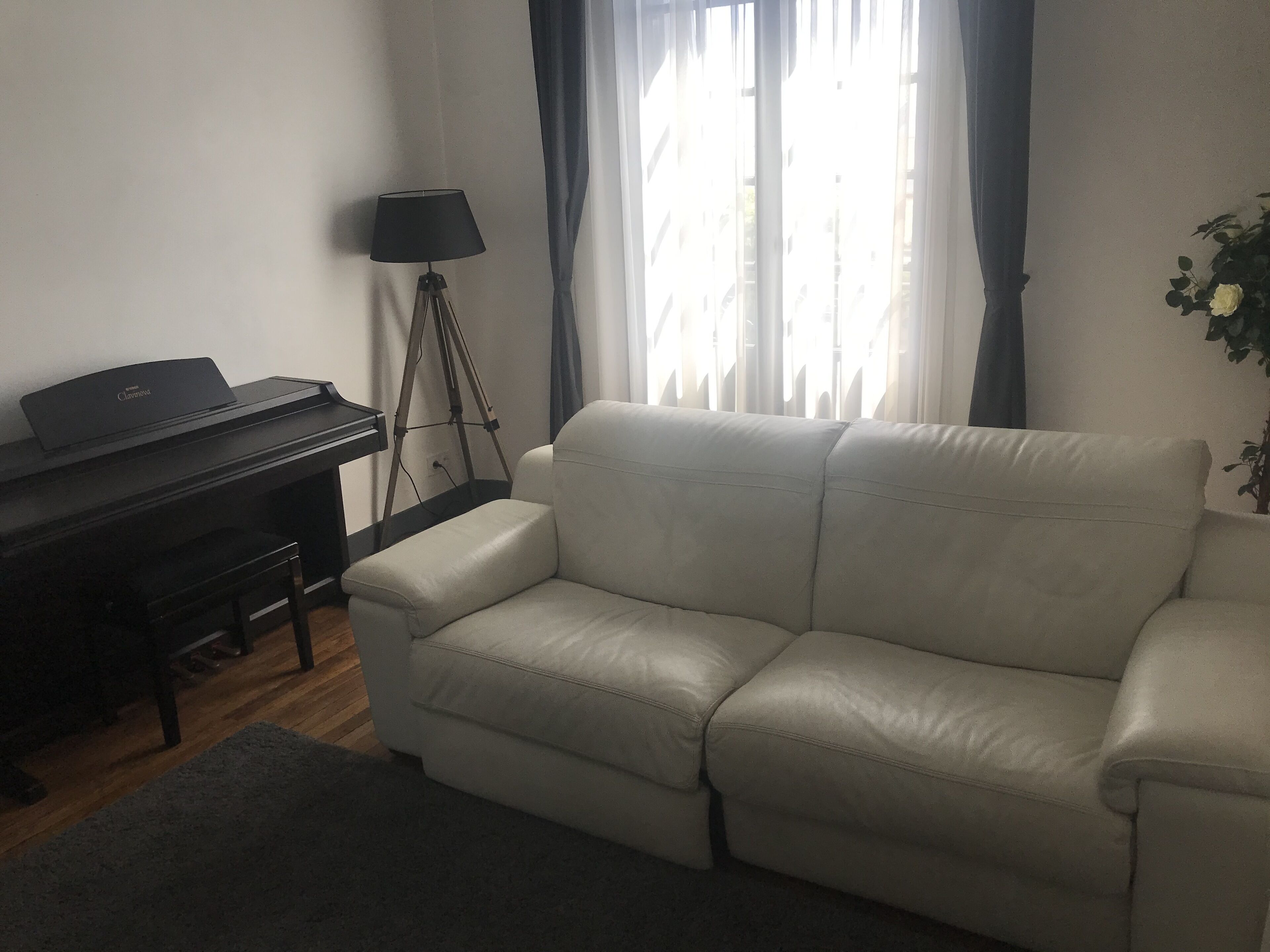A living room with a piano, a sofa, a lamp, and a window with curtains.
