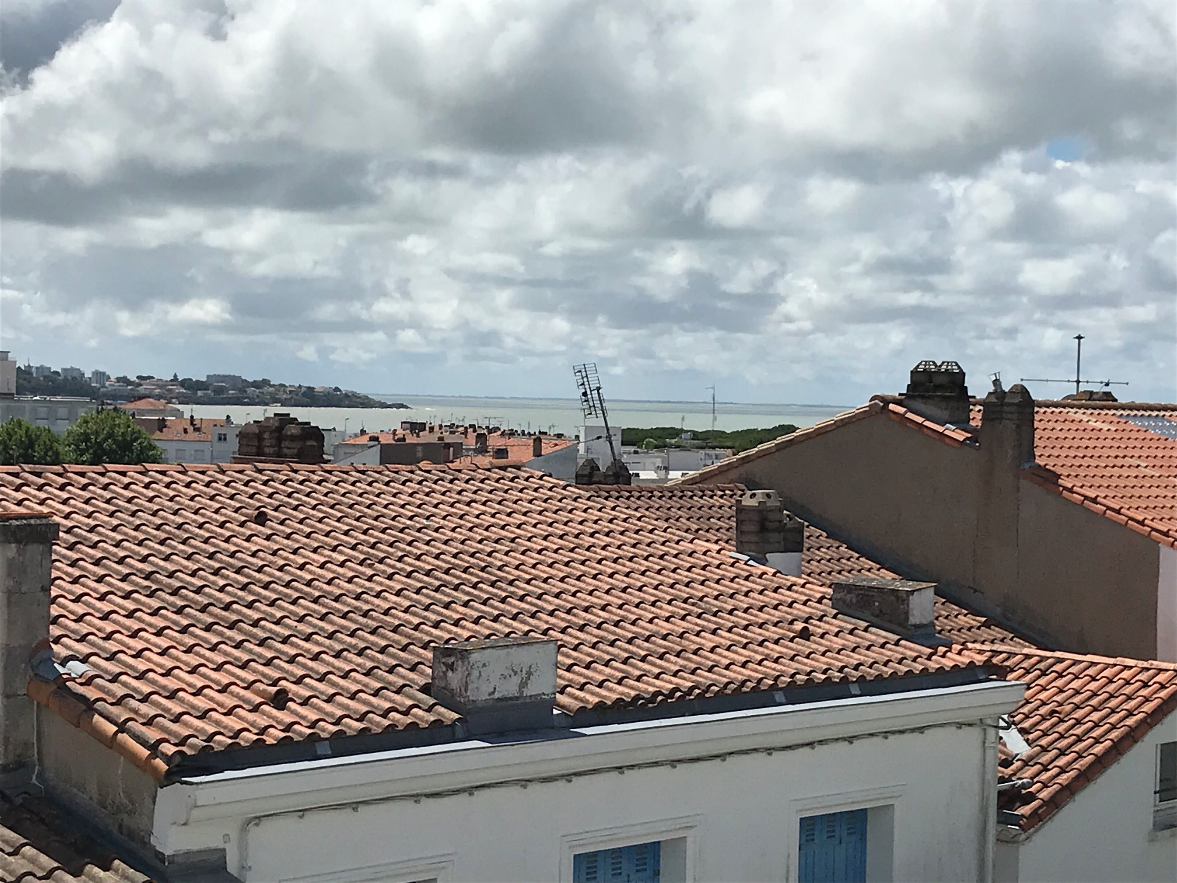 A view of terracotta-tiled rooftops, a body of water, and distant buildings under a cloudy sky.