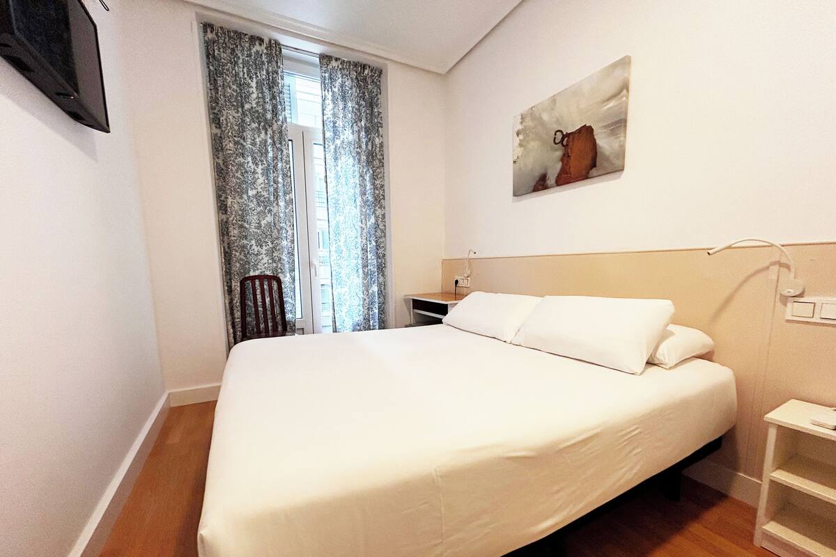 Una habitación de hotel con cama, una silla, un escritorio y un cuadro en la pared.