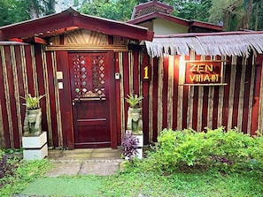 A wooden structure with a red door, a sign reading 'ZEN VILLA #1', and potted plants.