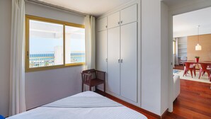 A hotel room with a bed, a chair, a wardrobe, and a view of the sea.