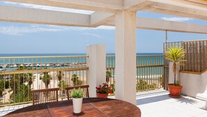 A balcony with a view of the beach and ocean, featuring a wooden table, potted plants, and a yellow ceiling.