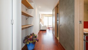 A hallway with wooden flooring, a blue flower pot, and a door leading to a room with a red accent wall.