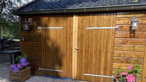 A wooden garage with two doors, metal handles, and two wall-mounted lanterns.