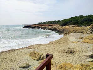 A sandy beach with rocky outcrops and a wooden railing.