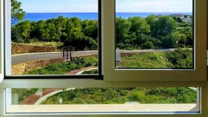 Vista a través de una ventana de un paisaje costero con árboles, un muro de piedra y una carretera.